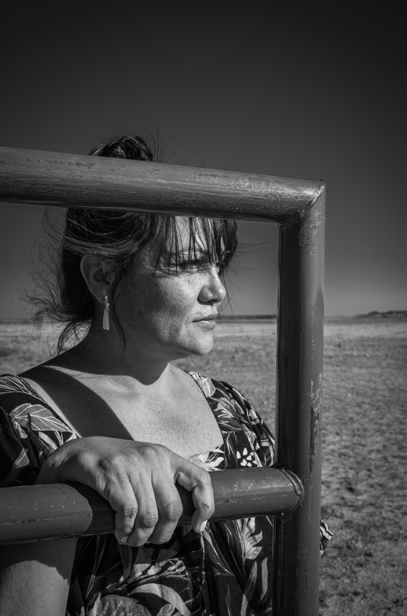 Patti Baldes, a member of the Northern Arapaho Tribe, stands next to the gate of a bison enclosure. Photo by Russel Albert Daniels/High Country News